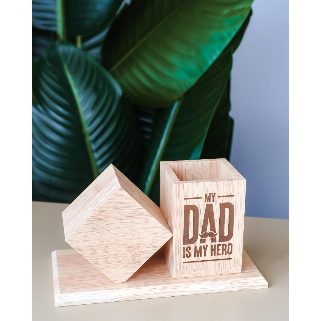 A light natural wooden desk clock with a matching geometric lid, with an attached pen holder engraved with the text 'MY DAD IS MY HERO'.