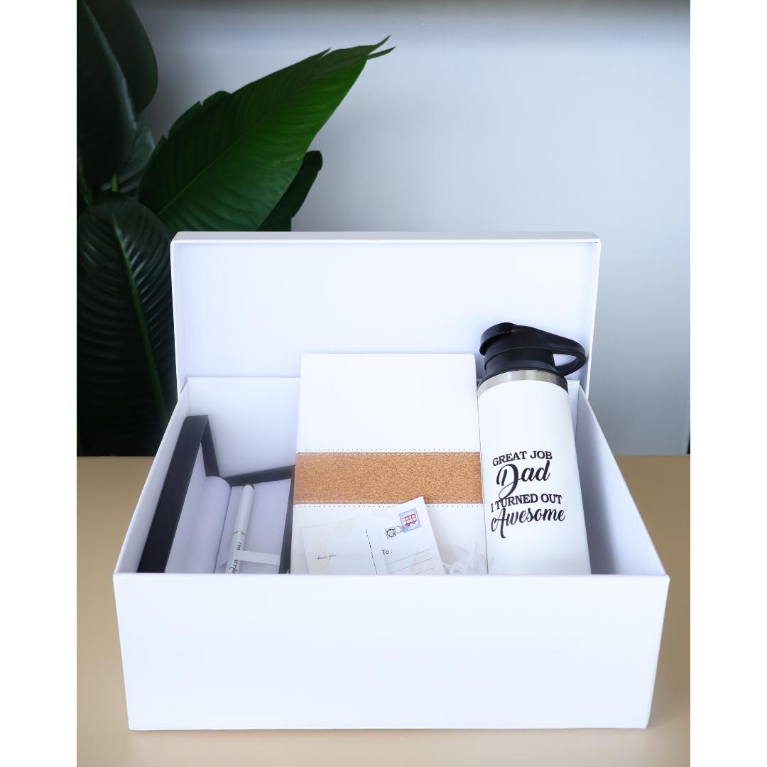 A father's day gift box containing a white insulated water bottle with a sentimental message for dad engraved on it, a white notebook, a small white card, and an extravagant pen case.