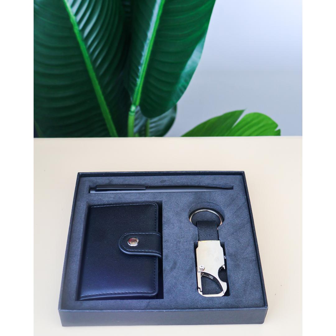 A dark navy blue leather gift set in a matching presentation box, featuring a wallet, a pen, and a keychain with a silver metal clip.