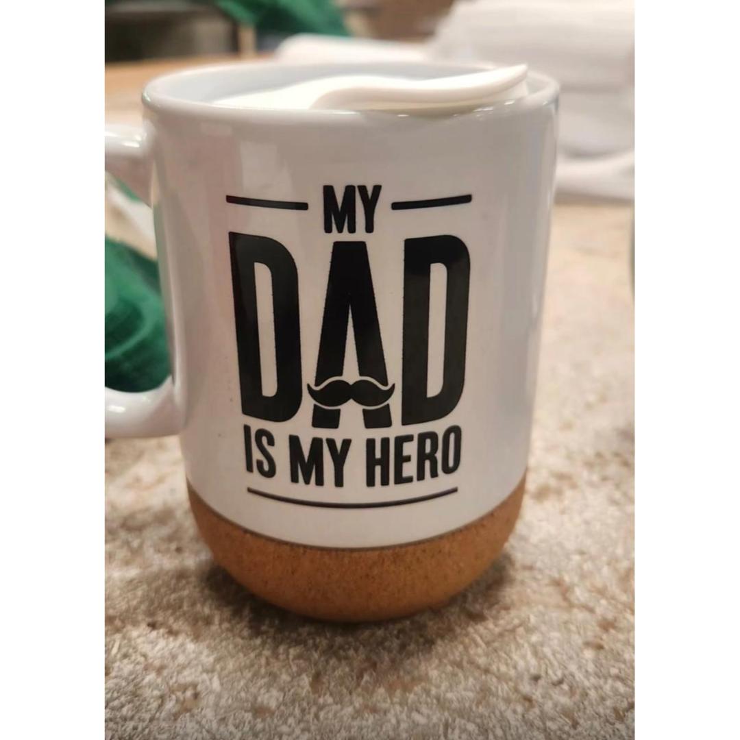 A white ceramic mug featuring the printed text 'MY DAD IS MY HERO' in black.