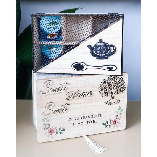 A decorative wooden tea gift box set with a lower wooden box engraved with 'Sweet Home IS OUR FAVORITE PLACE TO BE' and floral details, topped with a black metal wire organizer box holding tea bags and a teapot-shaped container.