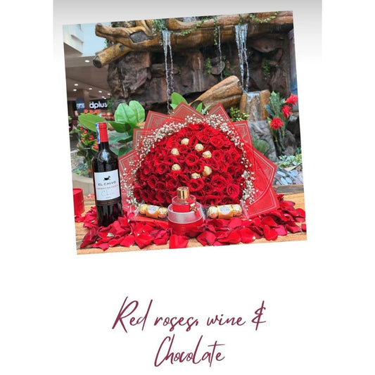 A red rose bouquet arrangement with a bottle of red wine and several chocolate-covered treats.