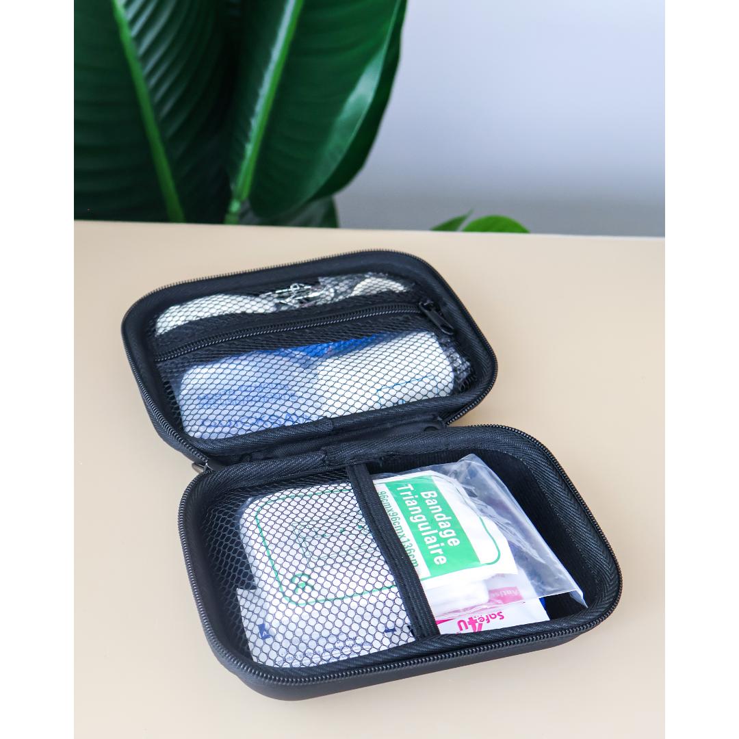 An open black zippered first aid kit case, showing mesh pockets with medical supplies including a green and white bandage packet and gauze.