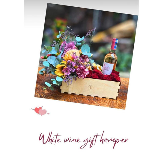A white wine gift hamper presentation showing a wooden crate filled with red roses, a bottle of white wine, and a colorful flower bouquet.